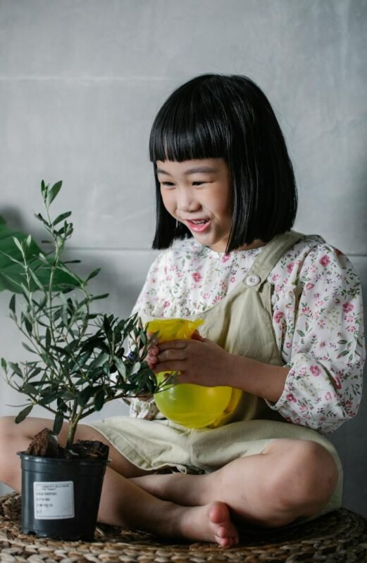 joyful ethnic kid watering potted plant at home