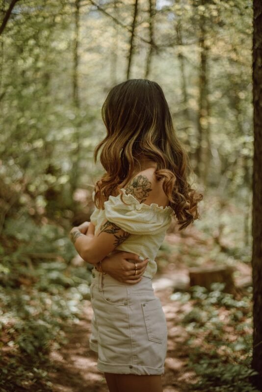 woman with tattoos embracing herself in forest