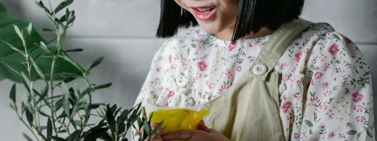 joyful ethnic kid watering potted plant at home