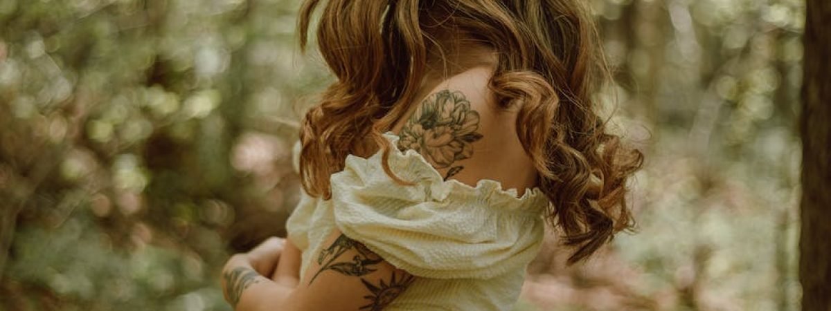 woman with tattoos embracing herself in forest