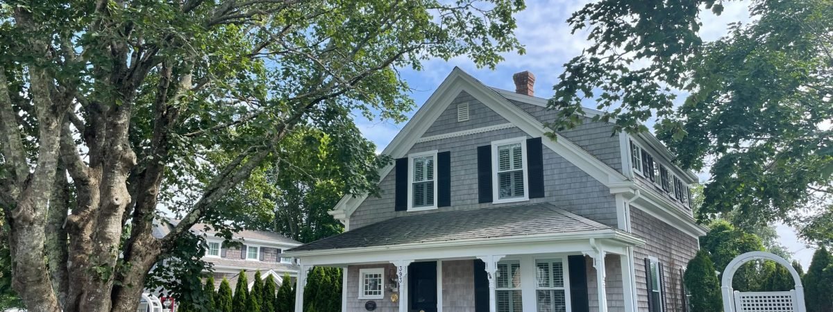 white and gray wooden house near green trees under white clouds during daytime